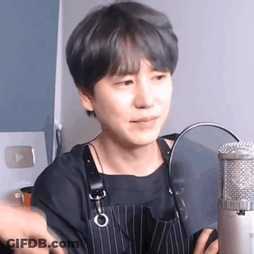 A Young Man Wearing An Apron Is Sitting In Front Of A Microphone And Making A Funny Face . GIF