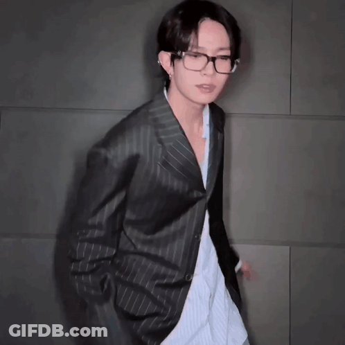 A Young Man Wearing Glasses And A Black Jacket Is Dancing . GIF