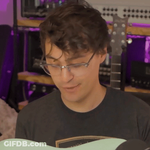 A Young Man Wearing Glasses And A Black Shirt Is Playing A Guitar GIF