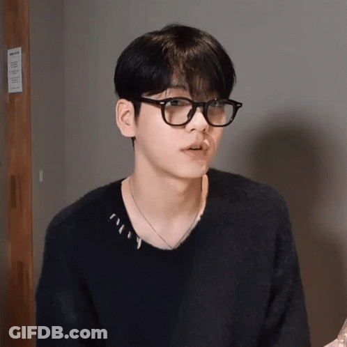 A Young Man Wearing Glasses And A Black Sweater Is Standing In Front Of A Sign That Says ' No Smoking ' GIF