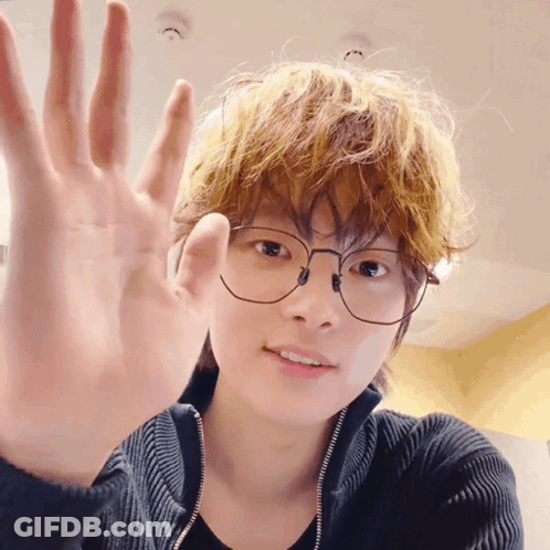 A Young Man Wearing Glasses And A Black Sweater Is Waving His Hand GIF