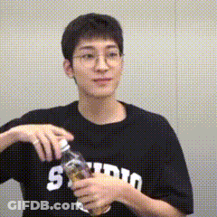 A Young Man Wearing Glasses And A Black T-Shirt Is Holding A Bottle Of Water . GIF