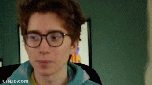 A Young Man Wearing Glasses And A Blue Hoodie Is Sitting In A Chair . GIF