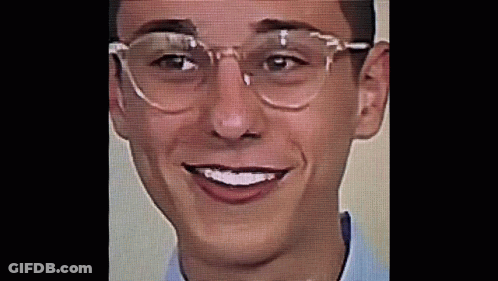 A Young Man Wearing Glasses And A Blue Shirt Is Smiling . GIF