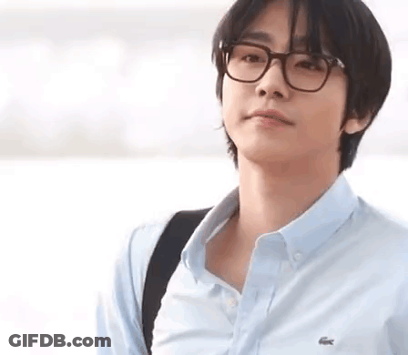A Young Man Wearing Glasses And A Blue Shirt Is Standing In Front Of A Body Of Water . GIF