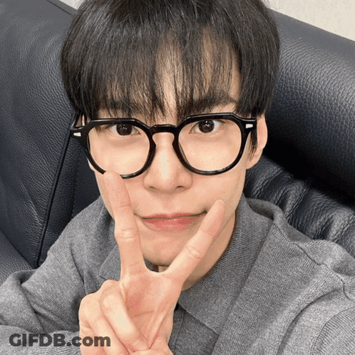 A Young Man Wearing Glasses And A Grey Shirt Giving A Peace Sign GIF