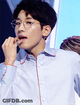 A Young Man Wearing Glasses And A Light Blue Shirt Is Eating Something GIF
