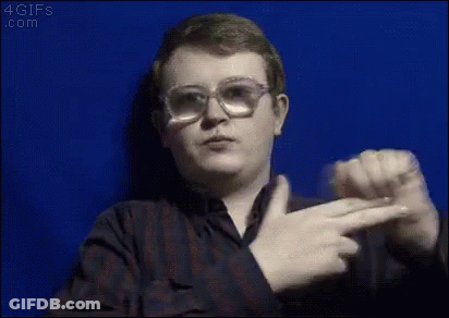 A Young Man Wearing Glasses And A Plaid Shirt Is Pointing At The Camera . GIF