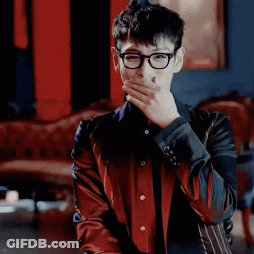 A Young Man Wearing Glasses And A Red Jacket Is Covering His Mouth With His Hand . GIF