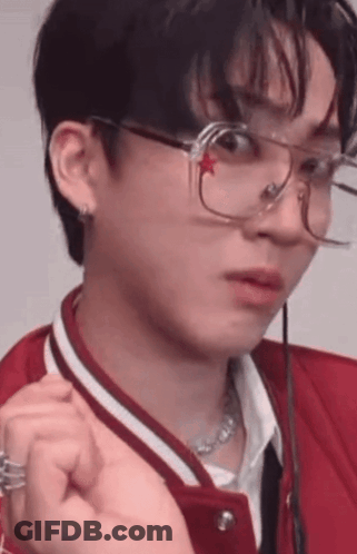 A Young Man Wearing Glasses And A Red Jacket Is Making A Face . GIF