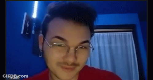 A Young Man Wearing Glasses And A Red Shirt Is Making A Funny Face . GIF