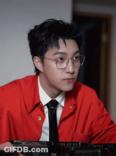 A Young Man Wearing Glasses And A Red Shirt Looks At Something GIF