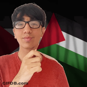 A Young Man Wearing Glasses And A Red Shirt Stands In Front Of A Flag GIF