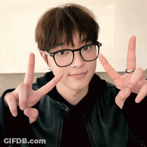 A Young Man Wearing Glasses And A Ring Is Giving The Peace Sign GIF