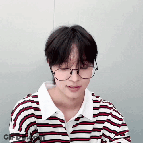A Young Man Wearing Glasses And A Striped Shirt Looks Down GIF
