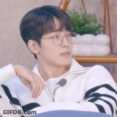 A Young Man Wearing Glasses And A Striped Sweater Holds A Pen GIF