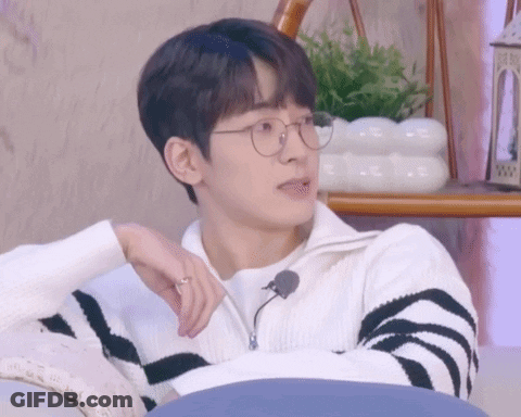 A Young Man Wearing Glasses And A Striped Sweater Is Sitting On A Couch With His Hand On His Chin . GIF