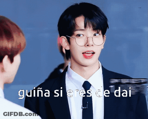 A Young Man Wearing Glasses And A Suit Is Talking To Another Man GIF