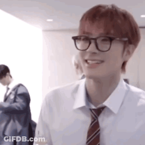 A Young Man Wearing Glasses And A Tie Is Smiling And Looking At The Camera . GIF