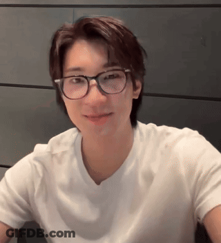 A Young Man Wearing Glasses And A White Shirt Looks At The Camera . GIF
