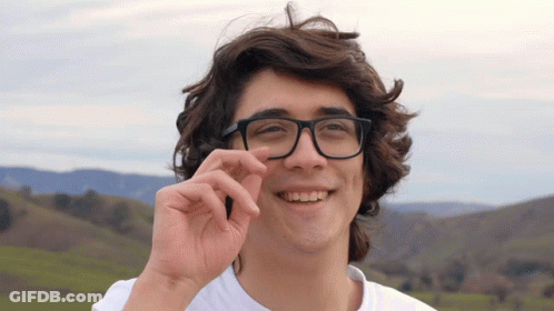 A Young Man Wearing Glasses And A White Shirt Smiles At The Camera GIF