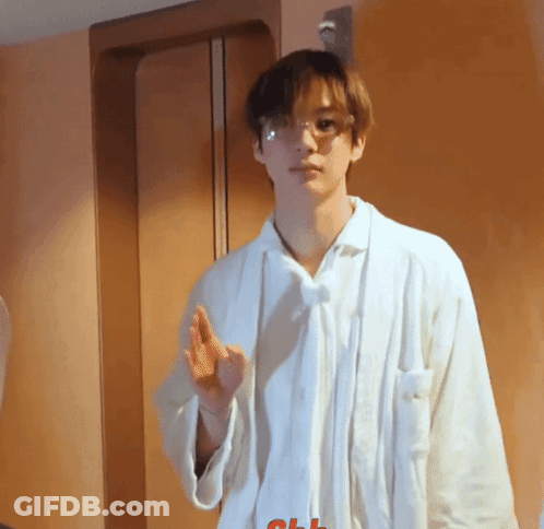 A Young Man Wearing Glasses And A White Shirt Stands In Front Of A Door GIF