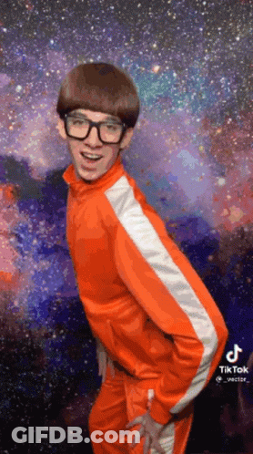 A Young Man Wearing Glasses And An Orange Jacket Is Dancing In Front Of A Galaxy . GIF