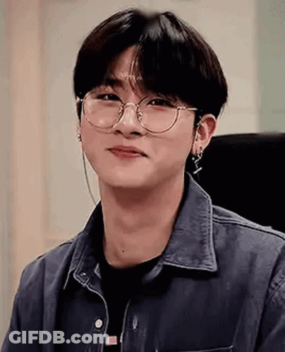A Young Man Wearing Glasses And Earrings Is Smiling . GIF