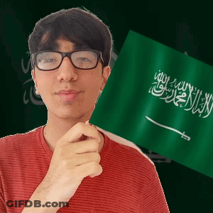 A Young Man Wearing Glasses Holds A Green Flag With Arabic Writing On It GIF