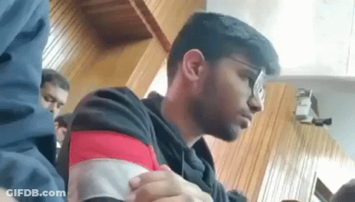 A Young Man Wearing Glasses Is Sitting At A Table In A Room . GIF