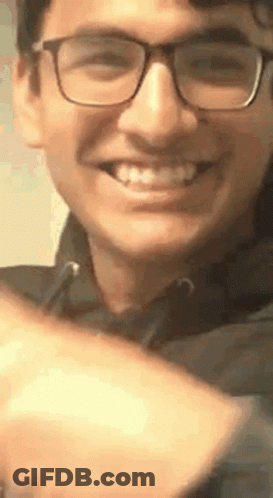 A Young Man Wearing Glasses Is Smiling And Making A Peace Sign . GIF