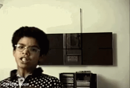 A Young Man Wearing Glasses Is Standing In Front Of A Stereo . GIF