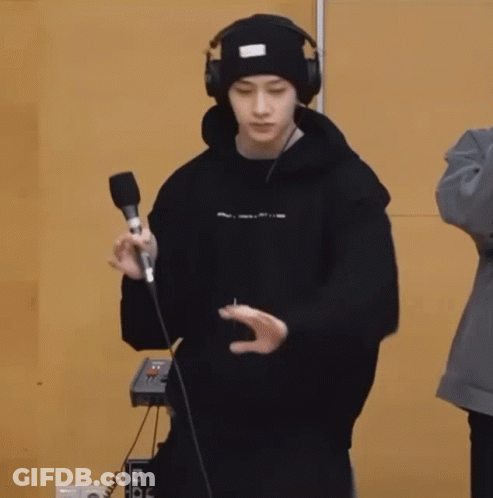 A Young Man Wearing Headphones And A Beanie Is Holding A Microphone And Dancing . GIF