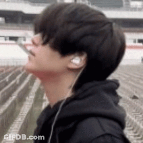 A Young Man Wearing Headphones And A Black Hoodie Is Smoking A Cigarette . GIF