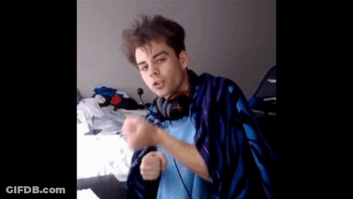 A Young Man Wearing Headphones And A Blue And Purple Blanket Is Sitting On A Bed . GIF