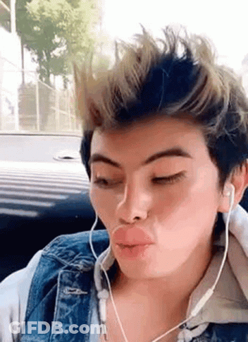 A Young Man Wearing Headphones And A Denim Jacket Is Making A Funny Face While Sitting In A Car . GIF