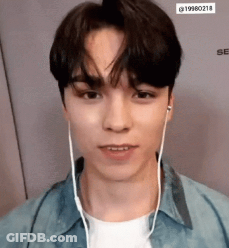 A Young Man Wearing Headphones And A Denim Shirt Looks At The Camera . GIF