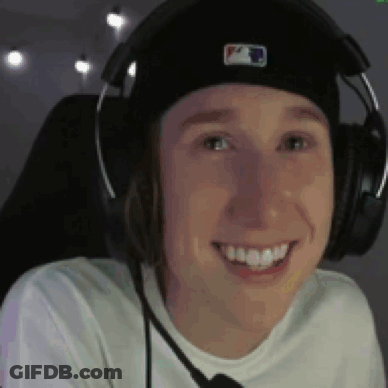 A Young Man Wearing Headphones And A Hat Is Smiling While Sitting In A Chair . GIF