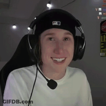 A Young Man Wearing Headphones And A Hat Is Smiling While Sitting In A Chair . GIF