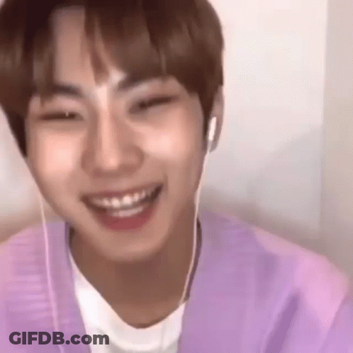A Young Man Wearing Headphones And A Purple Shirt Is Smiling And Looking At The Camera . GIF