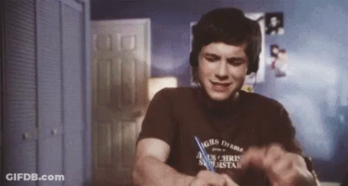 A Young Man Wearing Headphones And A T-Shirt Is Sitting At A Desk . GIF