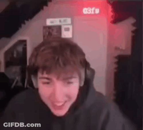 A Young Man Wearing Headphones Is Laughing While Looking At The Camera In A Room . GIF