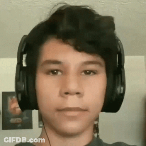 A Young Man Wearing Headphones Is Looking At The Camera In A Living Room . GIF