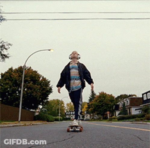 A Young Man Wearing Headphones Is Riding A Skateboard Down A Street GIF