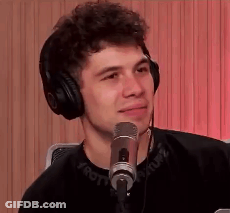 A Young Man Wearing Headphones Is Sitting In Front Of A Microphone And Smiling . GIF