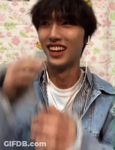 A Young Man Wearing Headphones Is Smiling And Clapping His Hands . GIF