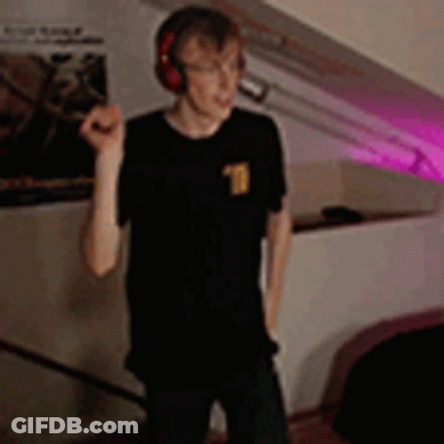 A Young Man Wearing Headphones Is Standing In A Room . GIF