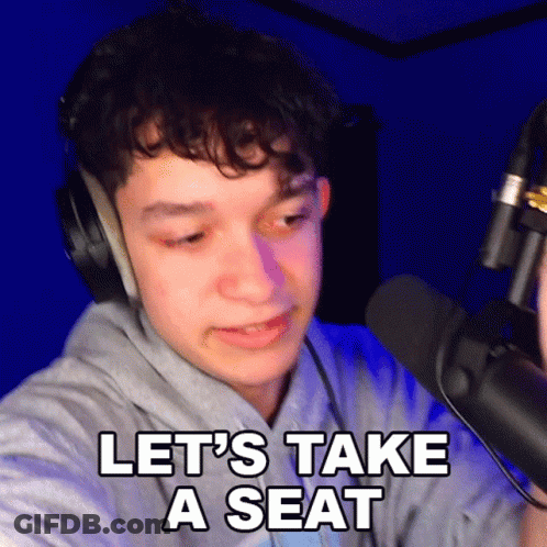 A Young Man Wearing Headphones Is Talking Into A Microphone And Says Let 'S Take A Seat GIF