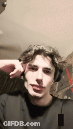 A Young Man Wearing Headphones Looks At The Camera With A Picture Of The Eiffel Tower In The Background GIF