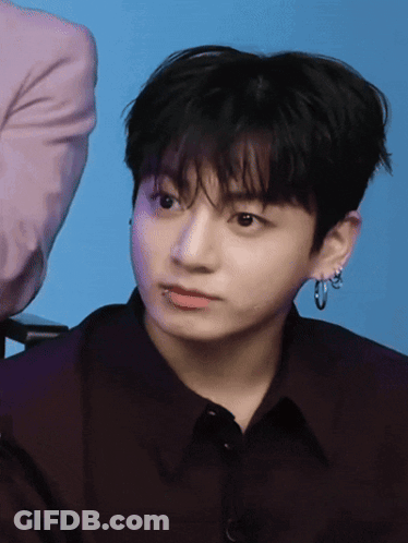 A Young Man Wearing Hoop Earrings And A Black Shirt Looks At The Camera GIF